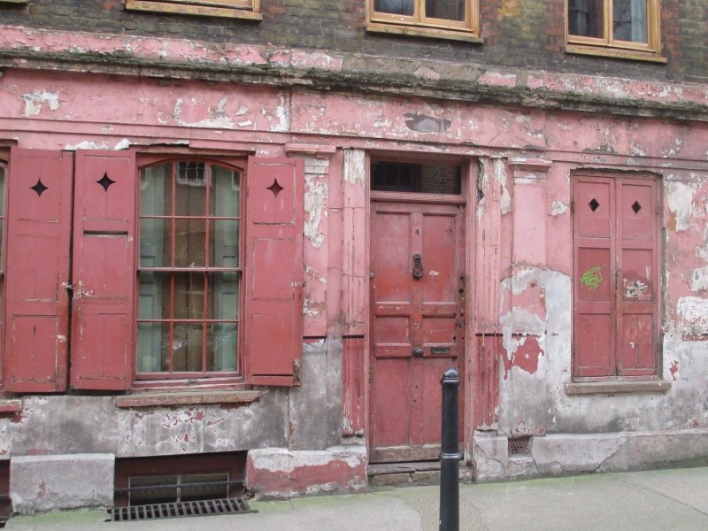 Old red outside house wall with three windows and one door